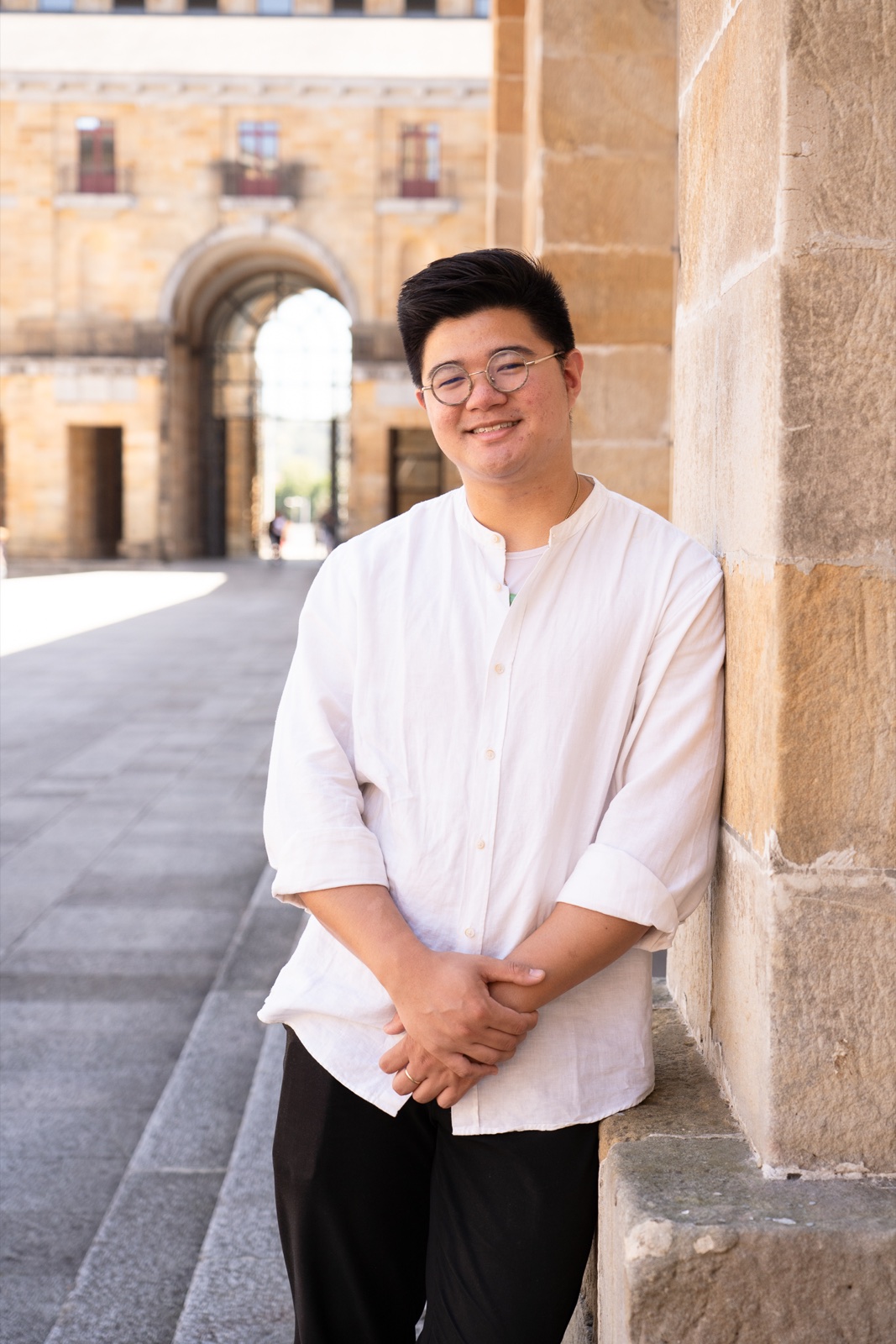 Stephen Joven-Lee smiling beside a stone column in Gijón, Spain
